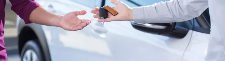 Des mains échangeant les clés d'une voiture blanche, symbolisant une location ou une vente.