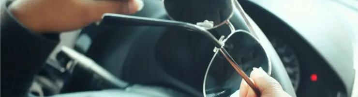 Gros plan sur des mains tenant des lunettes de soleil au-dessus d'un volant de voiture.