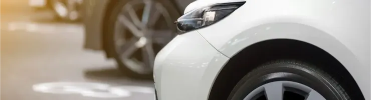 Gros plan sur l'avant d'une voiture blanche garée, avec d'autres véhicules flous derrière.