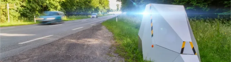 Un radar automatique sur le bord d'une route verdoyante, flashant une voiture en mouvement.