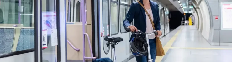 Une femme souriante sort d'un train dans une station de métro, tenant un vélo pliant.