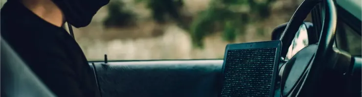 Un homme masqué tapant sur un ordinateur portable à l'intérieur d'une voiture.