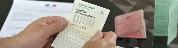 Mains tenant un certificat d'immatriculation français, avec d'autres documents et une clé.