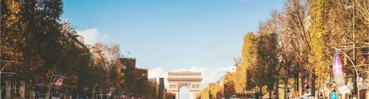 Vue large des Champs-Élysées animés à Paris, avec l'Arc de Triomphe en arrière-plan sous un ciel bleu.