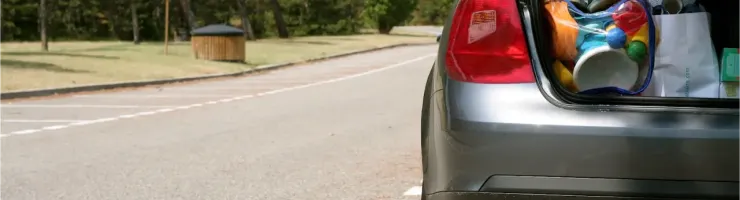 Le coffre d'une voiture grise rempli de sacs et d'articles, garée sur le côté d'une route.