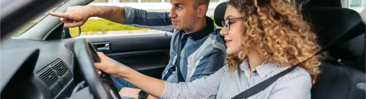 Un homme montre une direction à une jeune femme au volant d'une voiture.