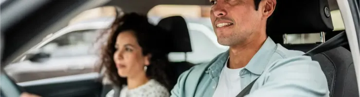 Un homme au volant d'une voiture, sa femme assise à côté de lui.