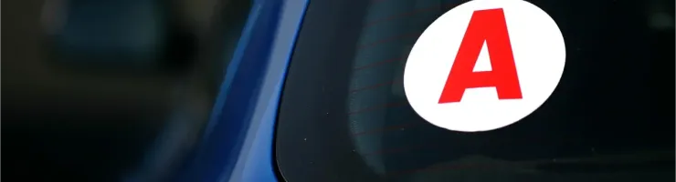 Gros plan d'un autocollant blanc avec un grand "A" rouge, signalant un jeune conducteur à l'arrière d'une voiture bleue.
