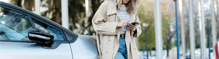 Une femme adossée à sa voiture consulte son téléphone.
