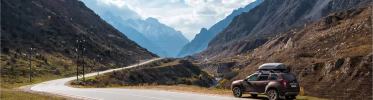 Un SUV marron avec un coffre de toit garé sur le bord d'une route sinueuse au milieu de montagnes imposantes.