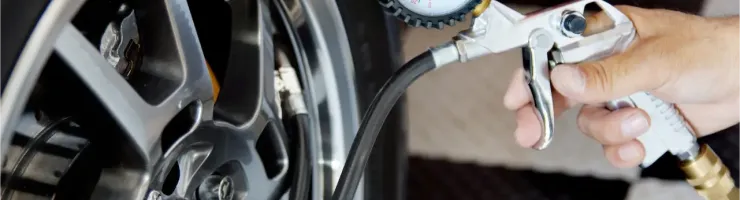 Une main gonfle un pneu de voiture avec un pistolet de gonflage et un manomètre sur une jante chromée.