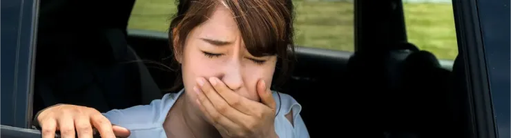Une jeune femme dans une voiture, la main devant la bouche, l'air nauséeux ou malade.