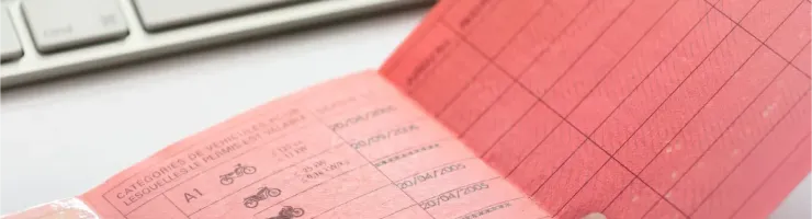 Gros plan d'un permis de conduire français en papier rose, avec une partie de clavier en arrière-plan.