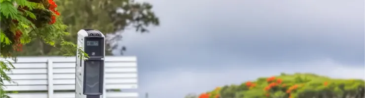 Un radar de vitesse gris et blanc sur le bord d'une route bordée d'arbres, sous un ciel couvert en France.