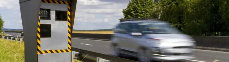 Un radar de vitesse gris et jaune sur le bord d'une autoroute, avec une voiture floue en mouvement.