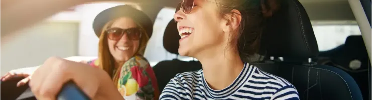 Deux jeunes femmes souriantes et heureuses dans une voiture, la conductrice rit aux éclats.