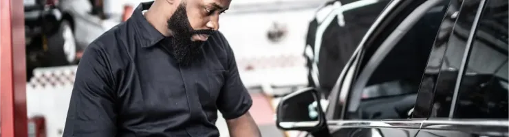 Un mécanicien barbu examine des documents à côté d'une voiture noire dans un garage.
