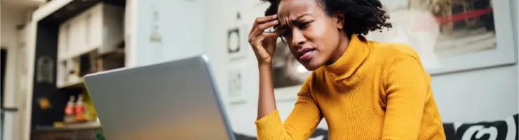 Une jeune femme, l'air stressé, regarde son ordinateur portable à la maison.