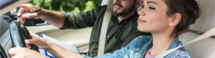 Une jeune femme souriante apprend à conduire, un instructeur attentif pointant quelque chose.