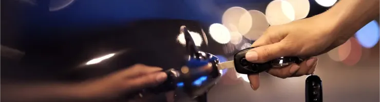 Une main ouvre la porte d'une voiture noire avec une clé, les lumières de la ville floues en arrière-plan.