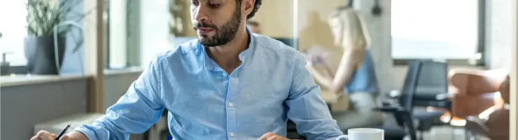 Un homme à son bureau, concentré sur sa tablette dans un environnement de bureau moderne.