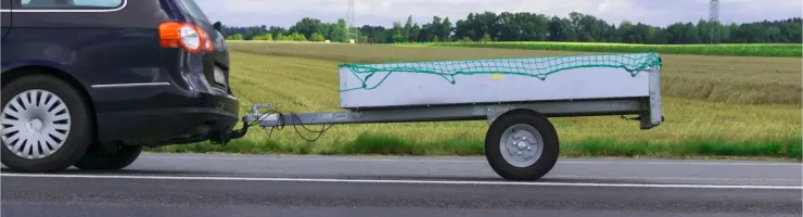 Une voiture noire tracte une petite remorque avec un filet vert sur une route, un champ en arrière-plan.