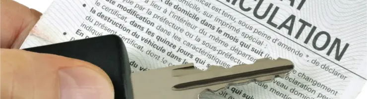 Une main tient une clé de voiture au-dessus d'un certificat d'immatriculation de voiture français.