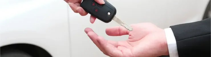 Deux mains échangent une clé de voiture devant un véhicule blanc, symbolisant le partage d'une voiture entre particuliers.