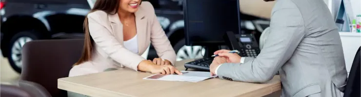 Une femme et un homme discutent de documents à un bureau dans ce qui semble être une concession automobile.