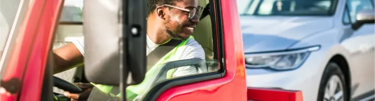 Un conducteur souriant dans un dépanneuse rouge, avec une voiture argentée à l'arrière.