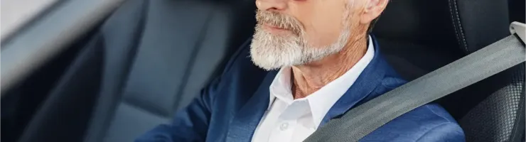 Un homme élégant, âgé, avec une barbe blanche et des lunettes de soleil, est assis dans une voiture.