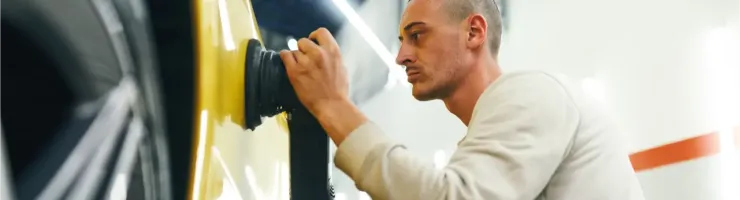 Un homme travaille méticuleusement sur la carrosserie d'une voiture jaune avec une polisseuse.