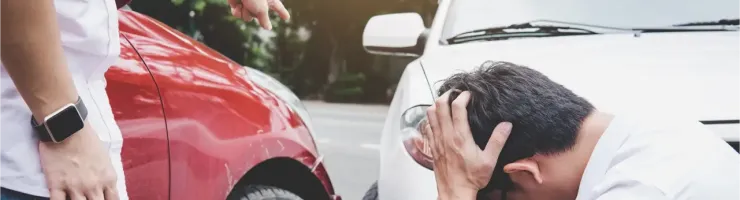 Deux hommes confrontent après un accident de voiture. L'un, en t-shirt rose, pointe du doigt un autre, désespéré, en t-shirt blanc.