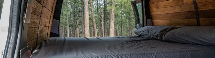 L'intérieur d'une camionnette aménagée en camping-car avec un lit et vue sur une forêt.