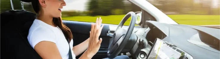 Une femme souriante dans une voiture avec les mains levées, utilisant un écran de navigation.