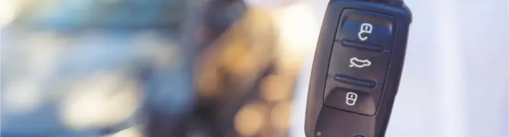 Une main tend une clé de voiture moderne avec télécommande, avec une voiture floue en arrière-plan.