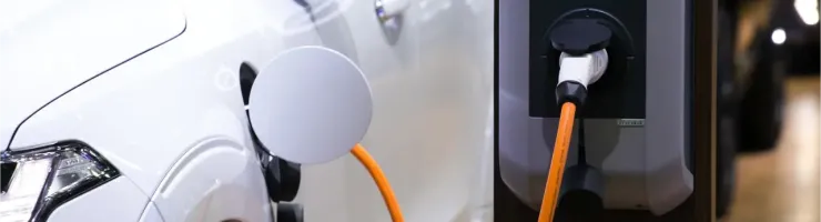 Gros plan d'une voiture électrique blanche en charge à une borne avec un câble orange.
