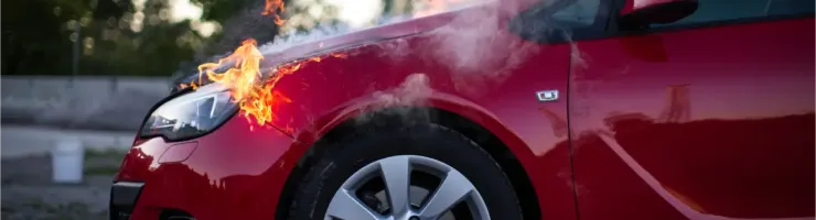 Une voiture rouge avec le capot en feu et de la fumée s'échappant.