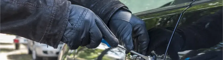 Des mains gantées utilisent un outil pour forcer la serrure d'une portière de voiture noire.