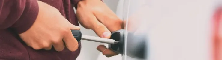 Gros plan de mains manipulant un tournevis pour ouvrir une poignée de portière de voiture blanche.