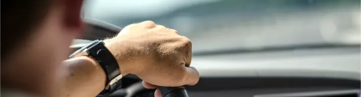 Gros plan d'une main sur un volant de voiture, avec la route floue en arrière-plan.