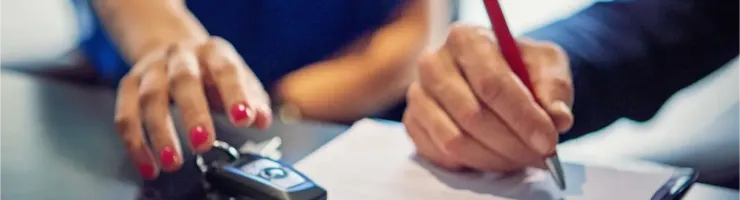 Gros plan d'une personne qui signe un contrat à côté d'une clé de voiture.