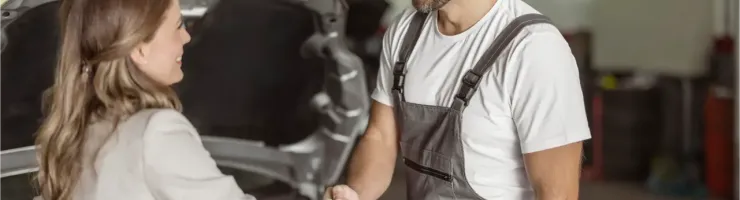 Un mécanicien souriant serre la main d'une cliente dans un garage automobile.