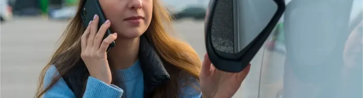 Une femme parle au téléphone et ajuste le rétroviseur latéral de sa voiture.