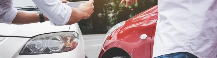 Deux personnes examinant les dégâts après un accident de voiture, l'une prenant une photo.