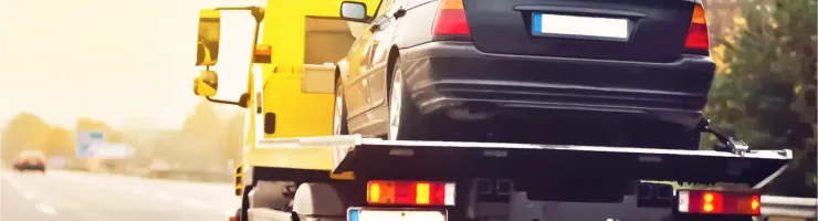 Une dépanneuse jaune transporte une voiture noire sur l'autoroute au coucher du soleil.