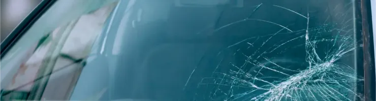 Gros plan sur un pare-brise de voiture blanc fissuré par des impacts.