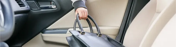 Une main prend un sac à main noir sur le siège passager d'une voiture.