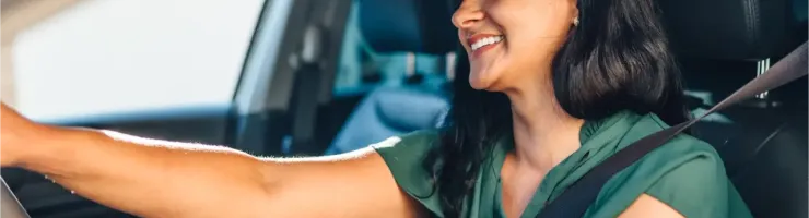 Une femme souriante et joyeuse conduit sa voiture avec la ceinture de sécurité attachée.