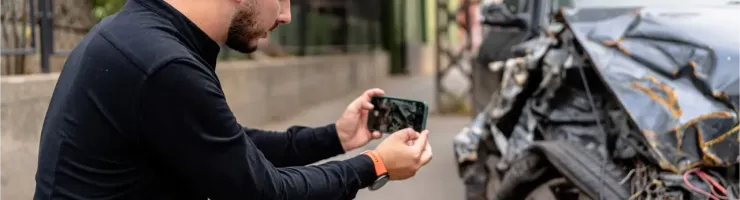 Un homme prend une photo d'une voiture gravement endommagée après un accident.